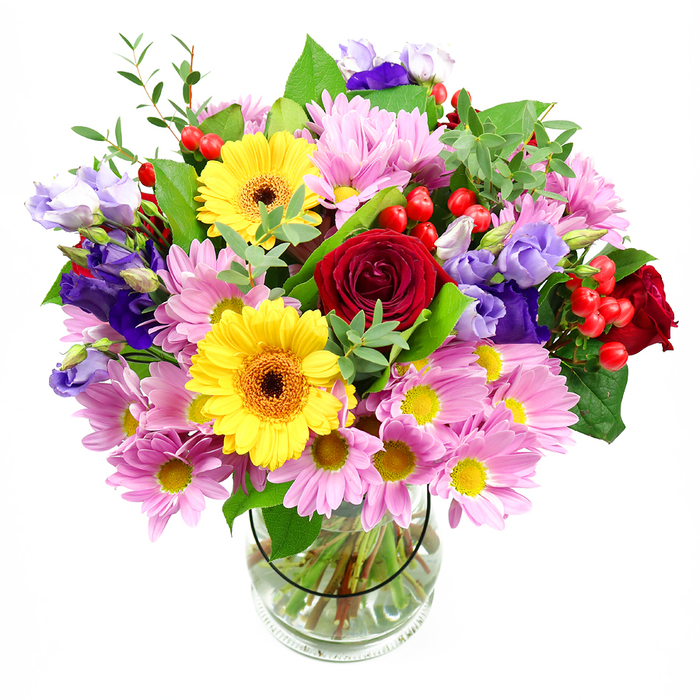 A tall glass vase holds a lush, carefully balanced bouquet of mixed blooms, all set against a spotless white background that highlights its varied textures and colours. At the centre, deep red roses unfurl their velvety petals, creating a rich, romantic focal point that draws the eye first. Just beside them, two bold yellow gerbera daisies with deep brown-orange centres seem to beam outward like small suns, flooding the arrangement with a sense of joy and positivity. Around these more dramatic flowers, clusters of soft pink daisies or chrysanthemums expand in every direction; each blossom has numerous delicate petals encircling a tiny yellow centre, forming a soft cushion of pastel colour that adds both volume and calm. Tall stems of purple and lavender lisianthus weave up through the bouquet, their bell-shaped flowers and elegant buds lending vertical movement and a cool counterbalance to the warmer tones. Bright red hypericum berries are tucked between leaves and petals, their rounded shapes and glossy surfaces creating playful dots of colour and a tactile contrast. The entire display is threaded with foliage in different shades of green, from broad, dark leaves offering structure to feathery, light-green sprigs that soften the edges and give a slightly wild, garden-fresh feel-something that might remind you of a stroll through nearby parks around Eastcote. Through the clear vase, neatly trimmed stems are visible, resting in clean water, evidence of professional preparation and care from Flowers Eastcote. The soft, even lighting reveals every nuance of tone without harshness. This mixed-colour bouquet feels perfect for marking a birthday, a thank-you, or a simple gesture of kindness, ready to brighten a dining table or office desk anywhere in the Eastcote area.